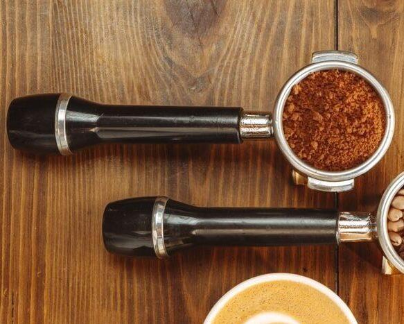 Espresso portafilters with coffee beans and latte art on wood surface.