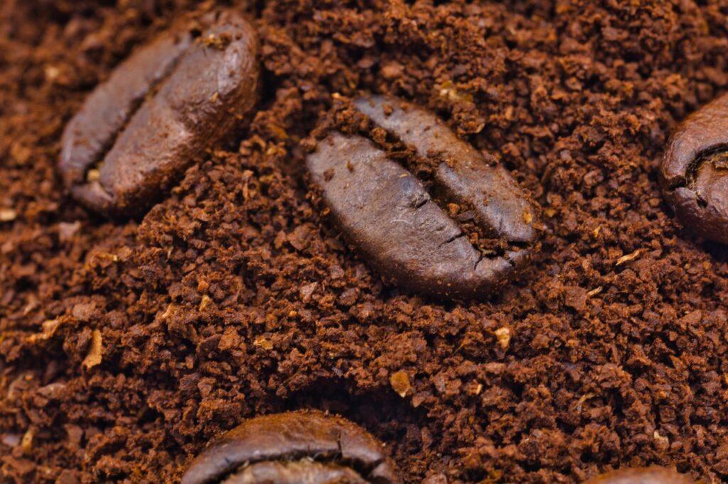 Macro shot of roasted coffee beans nestled in rich ground coffee, showcasing texture and aroma.