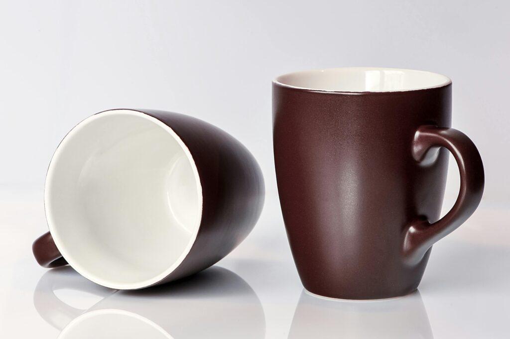 A pair of classic brown ceramic mugs displayed elegantly against a clean white backdrop, perfect for home and kitchen settings.
